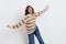 a cheerful woman stands on a white background in a striped sweater playfully depicts an airplane, turning in different