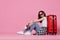 cheerful woman in sunglasses with red suitcase pink  background
