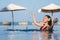 Cheerful woman in swimsuit playing water splashing in swimming pool with sea background