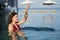 Cheerful woman in swimsuit playing water splashing in swimming pool with sea background