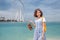Cheerful woman takes off her sandals and walks barefoot on the water on a beach with a view of the Dubai Eye Ferris Wheel