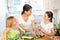 Cheerful woman with two little daughters prepare vegetable salad in the kitchen