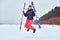Cheerful woman wearing warming sportswear jumping with skis on a snowy beach