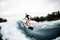 Cheerful woman in wetsuit rides down on surf style wakeboard on wave