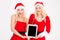 Cheerful women in santa cloth showing tablet computer screen