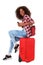 Cheerful young african american woman sitting on suitcase and laughing over white background