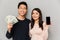 Cheerful young asian loving couple holding money and showing display of mobile phone.