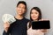 Cheerful young asian loving couple holding money and showing display of mobile phone.