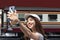 Cheerful young Asian woman traveler with backpack taking a photo or selfie in train station. Travel lifestyle concept