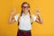 Cheerful young blonde female schoolgirl with pigtails in glasses shows thumbs up at free space