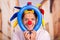 Cheerful young businessman with a red clown nose and colorful harlequin hut in his head playing with a blue ballons