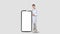 A cheerful young european doctor in a lab coat points to a blank smartphone screen