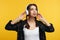 Cheerful young girl enjoy sound of music, keeps hands on headphones, isolated over yellow background