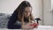 Cheerful young girl lying under blanket and typing on mobile phone in bed