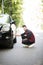 Cheerful young indian man has problems with the wheel of his car. He is kneeing and looking at it with seriousness