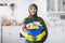 Cheerful young islamic housewife holding bucket with cleaning supplies