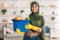 Cheerful young islamic housewife holding bucket with cleaning supplies tools