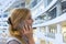 Cheerful young lady standing near glass wall of shopping center talking by phone. Pretty blondy young girl calling with smart