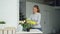 Cheerful young maid is dusting the furniture holding wet cloth and cleaning vase and table in modern light apartment