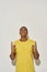 Cheerful young man in casual yellow t shirt looking and pointing index fingers up while posing isolated over gray