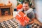 Cheerful young man embrcing his child and and smiling. He holds pesent that got from daughter. She wears red hat. They