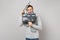 Cheerful young man in gray sweater, scarf hiding behind classic black film making clapperboard isolated on grey