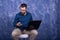 Cheerful young man working on laptop seated on a chair isolated over white background. Creative freelancer guy working from home