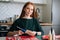 Cheerful young redhead woman gluing envelopes on board with gifts for children making Christmas advent calendar at home