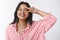 Cheerful young south-asian girl in striped blouse, smiling carefree, showing victory or peace sign over eye, grinning as