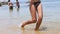 Cheerful young woman in bikini jumping in water at the beach on summer day.