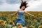 Cheerful young woman in a field of sunflowers jumping in a blue jeans dress. Freedom concept.