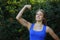 Cheerful young woman fitness shows inflated biceps in outdoors