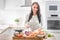 Cheerful young woman is happy to prepare lunch in her kitchen. She prepares food from meat and vegetables and other healthy