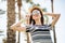 Cheerful young woman in hat and sunglasses hands over it in summer palms background. Summer vocation.