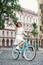 Cheerful young woman in light dress rides blue retro bicycle along the street block of the old city