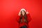 Cheerful young woman on a red background in New Year\'s clothes shows up for an offer, waiting for gifts