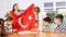 Cheerful young woman teacher demonstrating Turkish flag for schoolkids preteens during lesson of geography in auditory