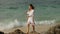Cheerful young woman in a white dress walks along some tropical island seashore