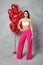 Cheerful young woman in wide bright pink trousers and white top posing next to balloons