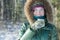 Cheerful young woman in winter forest holding stainless steel thermos flask tourist cup outdoors