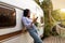 Cheery Asian lady leaning on motorhome, using cellphone on autumn camping trip in countryside