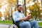 Cheery disabled black guy in wheelchair using mobile phone, checking email or messages at autumn park