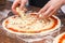 Cheese being spread on tomato sauce on pizza base