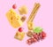 Cheese, breadsticks, grapes and walnut falling against light pink background