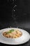 Cheese falling on pasta. Spaghetti with bacon, parmesan, cream sauce and egg yolk on black marble background