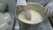 Cheese maker pours mass from pan into bags with net to remove whey.