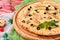 Cheese pizza with chicken and olives on a round wooden board on a red wooden background, decorated with napkins