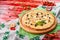 Cheese pizza with chicken and olives on a round wooden board on a red wooden background, decorated with napkins