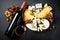 Cheese platter with craft cheese assortment on slate board at black background.