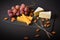 Cheese platter with hard and soft cheese pieces, grape, almonds on black slave stone board served with fruit forks